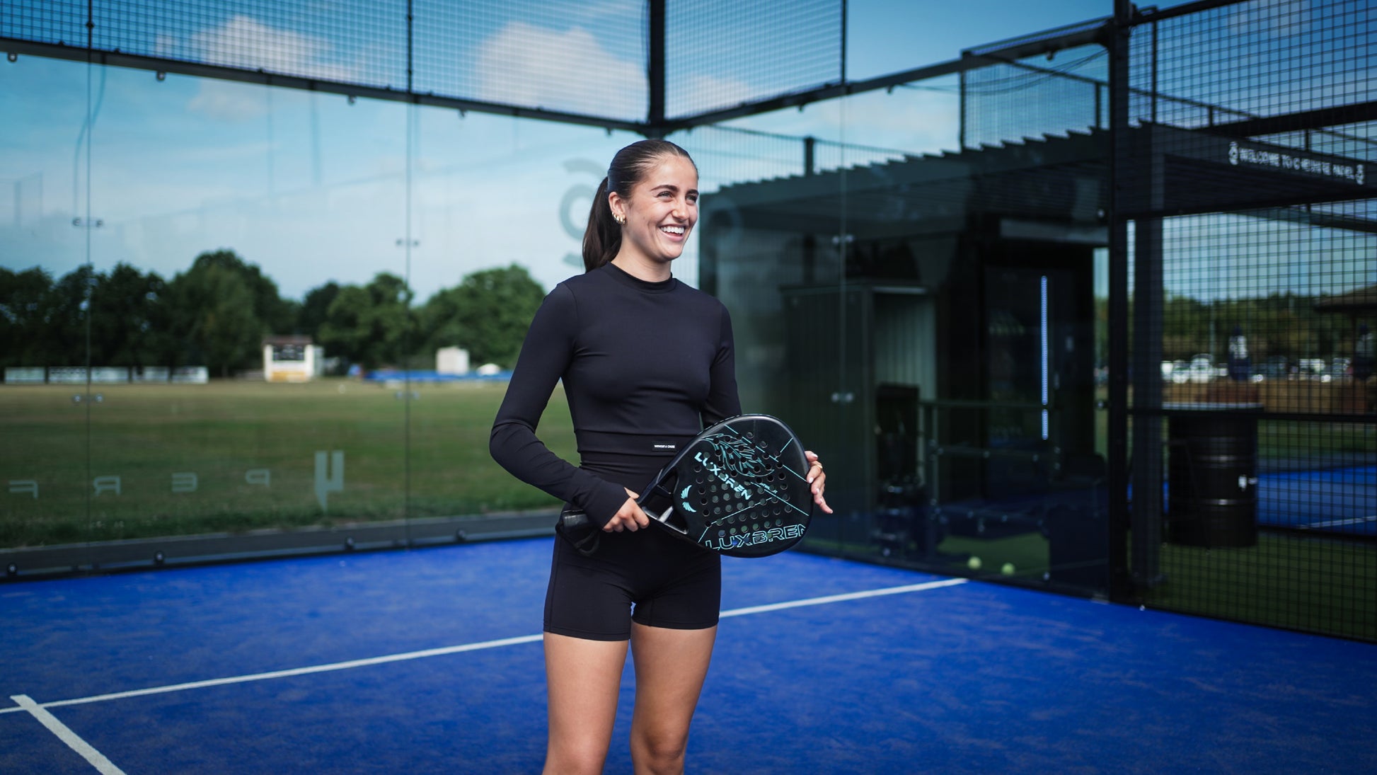Woman holding a padel racket with Luxbren branding on an outdoor padel court
