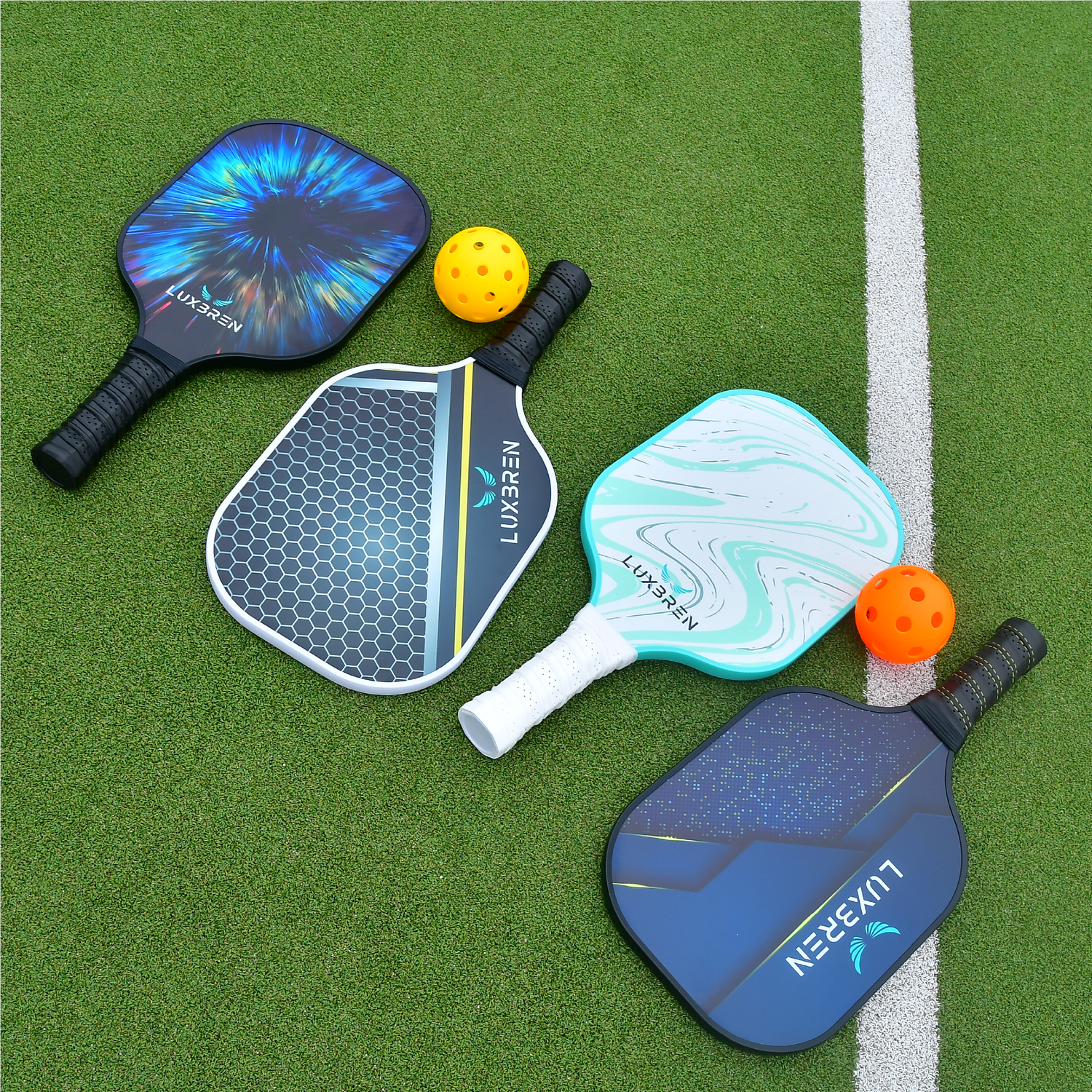 4 Luxbren pickleball paddles with different colours and designs on a green outdoor tennis court